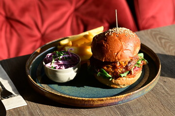 Juicy burger served with golden French fries on a plate in a restaurant setting. A classic and appetizing meal, perfect representation of comfort food and casual dining.