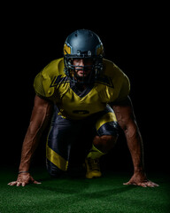 Strong American football athlete in yellow gear kneeling on grass, symbol of determination and power. Great for sports media, motivational design and championship themes.