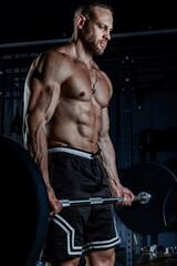 Muscular man having training with weights. Strong athletic man does workout. Concept bodybuilder doing exercises in gym.