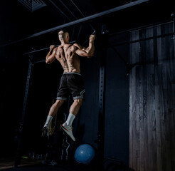 Muscular man training with weights. Brutal strong athletic men pumping up muscles workout in dark gym.