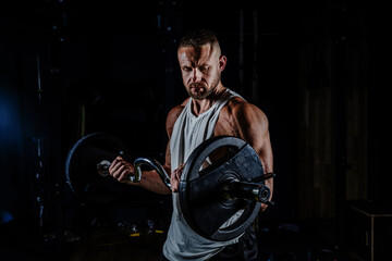 Muscular man training with weights. Brutal strong athletic men pumping up muscles workout in dark gym.