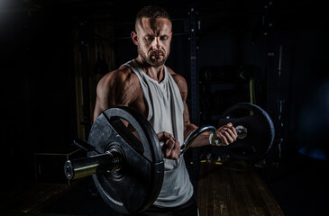 Muscular man training with weights. Brutal strong athletic men pumping up muscles workout in dark gym.