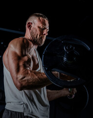 Muscular man training with weights. Brutal strong athletic men pumping up muscles workout in dark gym.