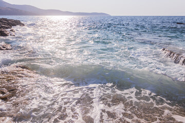 Sunlit turquoise shallows ripple gently against a rugged rocky coastline. The scene blends luminous water clarity with the timeless texture of coastal stone, evoking peace, warmth, and natural beauty.