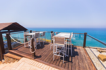 Modern seaside terrace with dining tables and chairs overlooking the ocean, perfect for luxury travel, summer holidays, tourism, and coastal lifestyle concepts.