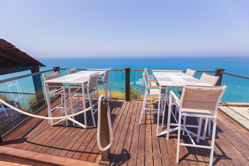 Modern seaside terrace with dining tables and chairs overlooking the ocean, perfect for luxury travel, summer holidays, tourism, and coastal lifestyle concepts.