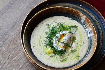 Top-down close-up view of a creamy soup with dill and egg, served in a restaurant. A traditional...