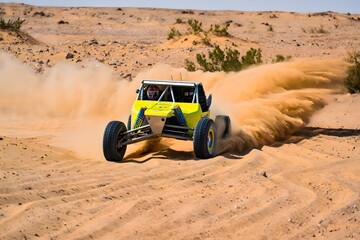 Off road vehicle driving through the desert with sand flying behind it in the bright sunshine