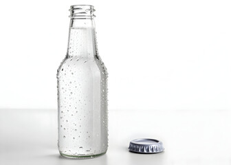 Chilled beverage bottle with condensation and a metal cap sits on a white surface