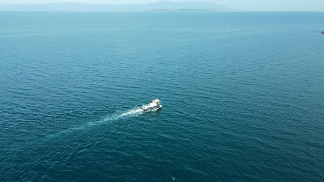 Workboat transiting between circular sea cages, aerial drone view. Feeding operations at the pens.