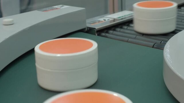 Demo making of Cosmetic cream jars move along automated conveyor belt in modern factory. Industrial production line concept  automation packaging manufacturing and mass production technology. close up