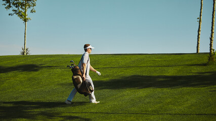 Golfer walking on green field with golf bag under blue sky. Concept of sports lifestyle, leisure,...