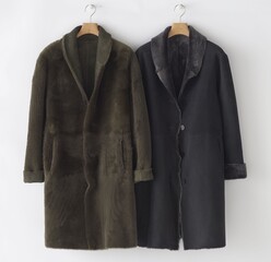 Two stylish long shearling coats hanging against a white background