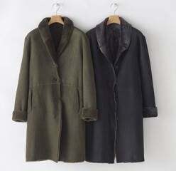 Two elegant sheepskin coats hanging against a white background studio shot