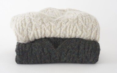 Stacked wool sweaters featuring cable knit pattern on white background