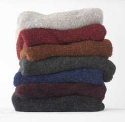 Stacked colorful folded wool sweaters in pile on white background