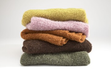 Stack of soft knitted sweaters in various colors on a white background