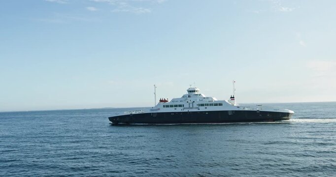 Passenger car ferry underway at sea, side view of modern vessel leaving white wake on open water under blue sky, maritime transport