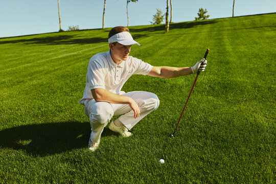 Golfer crouching on green analyzing ball position with concentration. Concept of focus, preparation, sports training, lifestyle and mindful performance in golf.