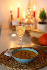 Plate of pumpkin soup, pumpkins, glass of wine, nuts and lit candles on the table. Selective focus. 