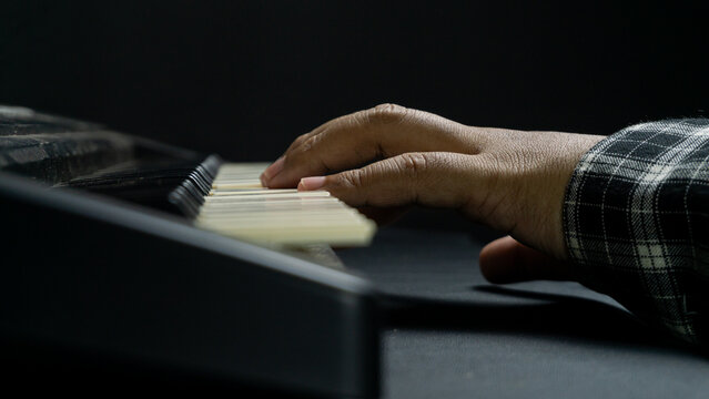 Piano played casually with one hand from side angle, dark monochrome setting, concept of relaxation, hobby, creativity, and minimalistic artistic musical scene.