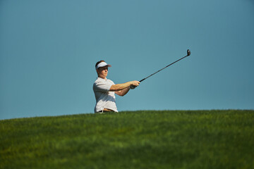 Golfer completing swing with club against clear sky. Concept of balance, precision, sport lifestyle, relaxation, outdoor health, and personal discipline.