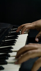 Piano played with two hands seen from slightly elevated diagonal angle in portrait orientation, dark setting, concept of creativity, art, harmony, and performance.