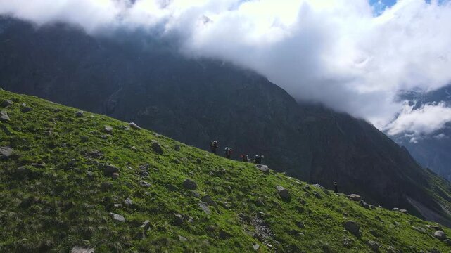 Slow drone approach across alpine meadow to the huge Mizhirgi icefall in Bezengi, Caucasus. Clear summer weather, rugged cliffs and moving cloud create cinematic landscape for travel content