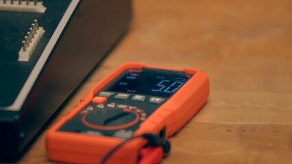 Close-up of a digital multimeter on a wooden workbench used for measuring voltage. Ideal for engineering, electronics, testing, and electrical diagnostics themes.