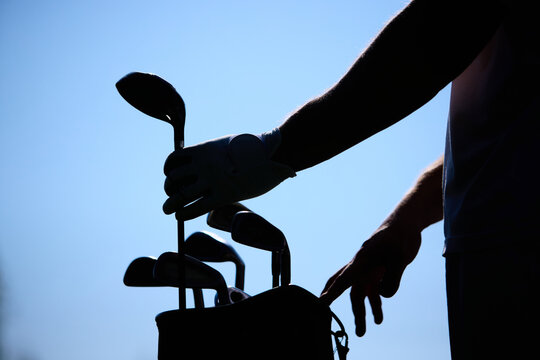Golfer silhouette selecting club from bag on clear blue sky background. Concept of sports lifestyle, leisure, active outdoor recreation and mental balance in golf. - Powered by Adobe