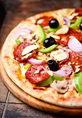 Pizza with chorizo ​​sausage, mozzarella cheese, green pepper and black olives. Rustic wooden background. Soft focus.	