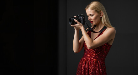 Young woman photographing with camera in red dress on dark background  