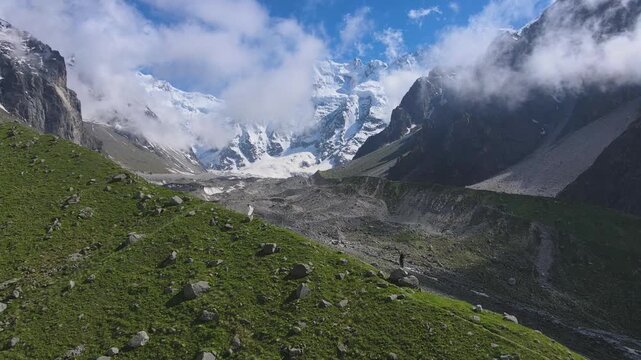 Aerial view glides toward the Mizhirgi glacier framed by dark cliffs in Bezengi, Caucasus. Clouds part to reveal crevasses and fresh snow, highlighting alpine geology and dramatic mountain landscape