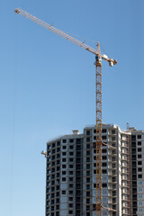 Obraz premium Low-angle view of tall tower crane above unfinished residential high-rise building against clear blue sky, symbolizing urban development, progress, and engineering.