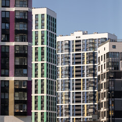 Fototapeta premium Vibrant cityscape featuring colorful high-rise residential buildings with glass balconies, modern architecture, and clear blue sky during golden hour.