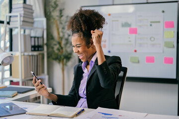 Excited african american businesswoman celebrating success while looking at smartphone in office