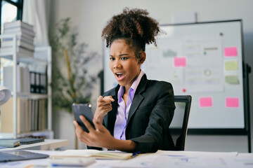 Shocked African American businesswoman pointing at smartphone in office