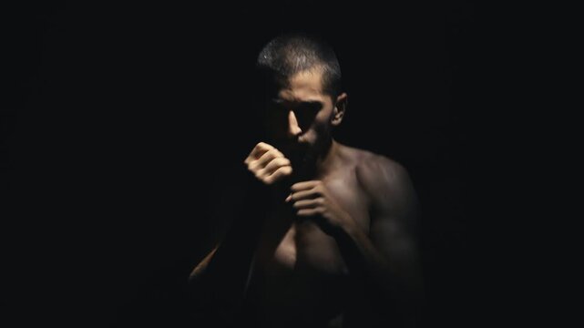 Athletic man in a dynamic boxing stance, showcasing powerful movements and intense focus, captured in a dramatic low-light setting, emphasizing strength and determination