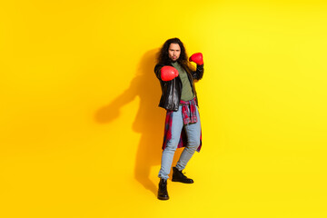 Dynamic portrait of young man posing confidently with red boxing gloves against bold vibrant yellow...