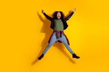 Energetic young man with long hair jumping on a bright yellow background, showcasing casual fashion and stylish trends