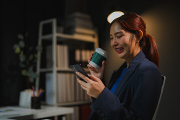 Businesswoman drinking coffee and using smartphone in office at night