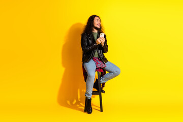 Young fashionable man with a smartphone sitting casually on a stool in front of a bold yellow...