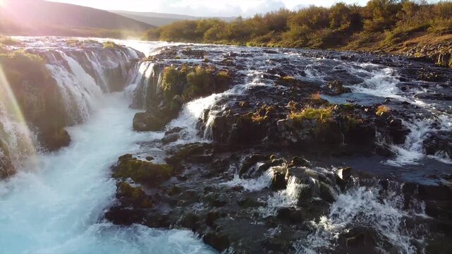 Low Drone Flight Along River Toward Br&uacute;arfoss Waterfall with Sun Flare