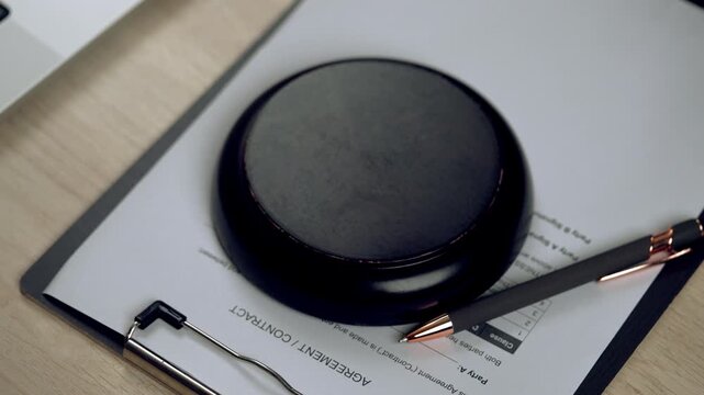 Close-up of hand signing legal document with gavel and pen on table, representing business agreement, law, and corporate approval.