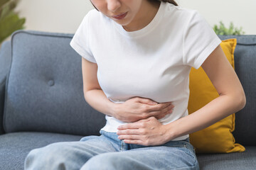 Sick asian young woman in pain, hand holding belly, stomach pain from food poisoning, girl hurt...