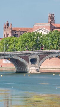 Garonne River and Pont Neuf timelapse with Basilica of Our Lady of the Daurade in downtown Toulouse, France. Renaissance arch bridge reflects in the water under a blue sky. Waterfront with green trees