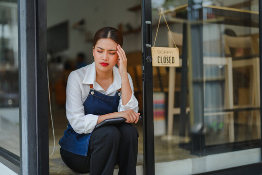 Stressed waitress sitting in front of closed coffee shop holding tablet
