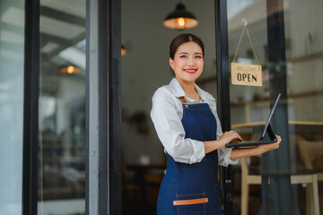 Smiling waitress using tablet at restaurant entrance with open sign