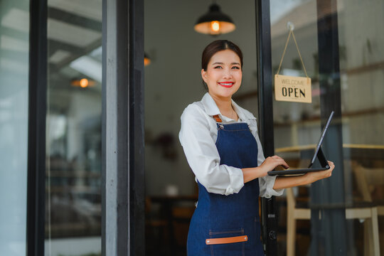 Smiling waitress using tablet at restaurant entrance with open sign