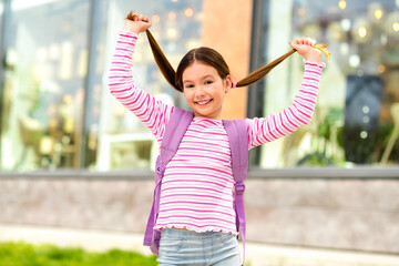 Cheerful young girl with brown hair in striped shirt enjoying outdoor activities in urban setting